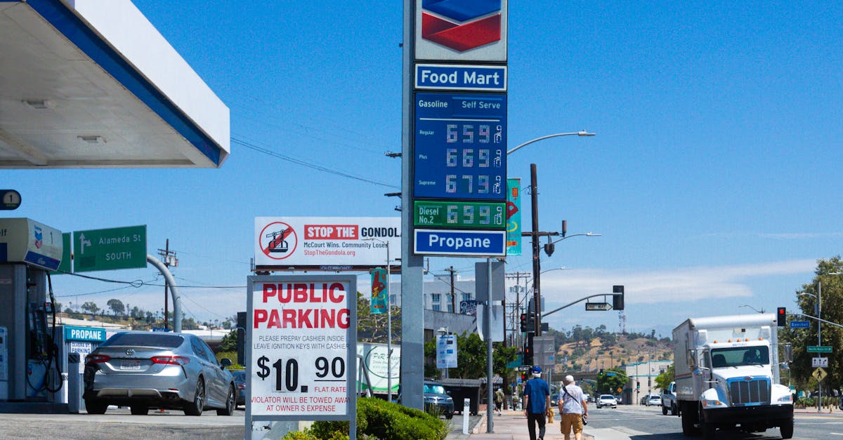 Shoppers walk past a Chevron gas station with fuel price signage on a clear day