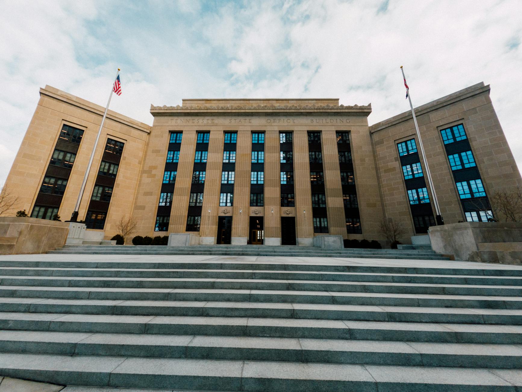 The Federal Reserve building in Washington, viewed from below against US flags and a cloudy sky