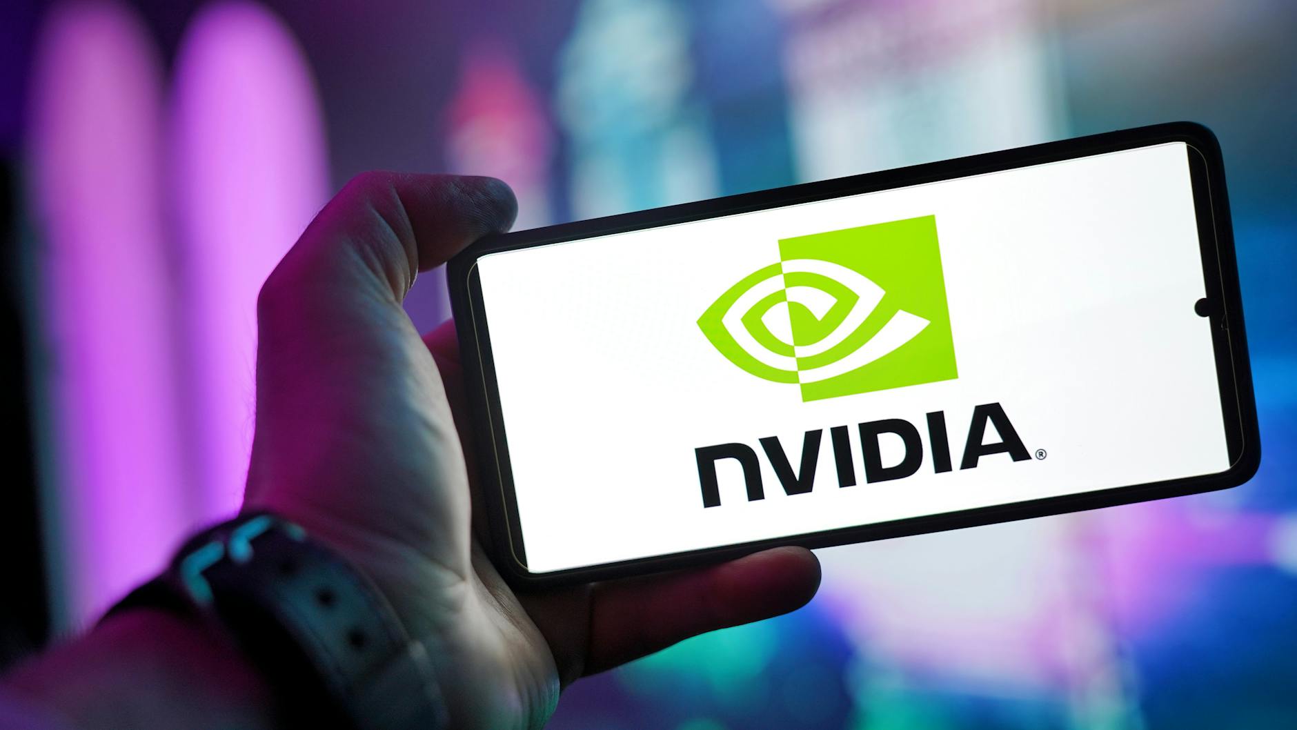 Hand holding a smartphone displaying the Nvidia logo, illustrating the chipmaker's growing equity stakes in AI customers.