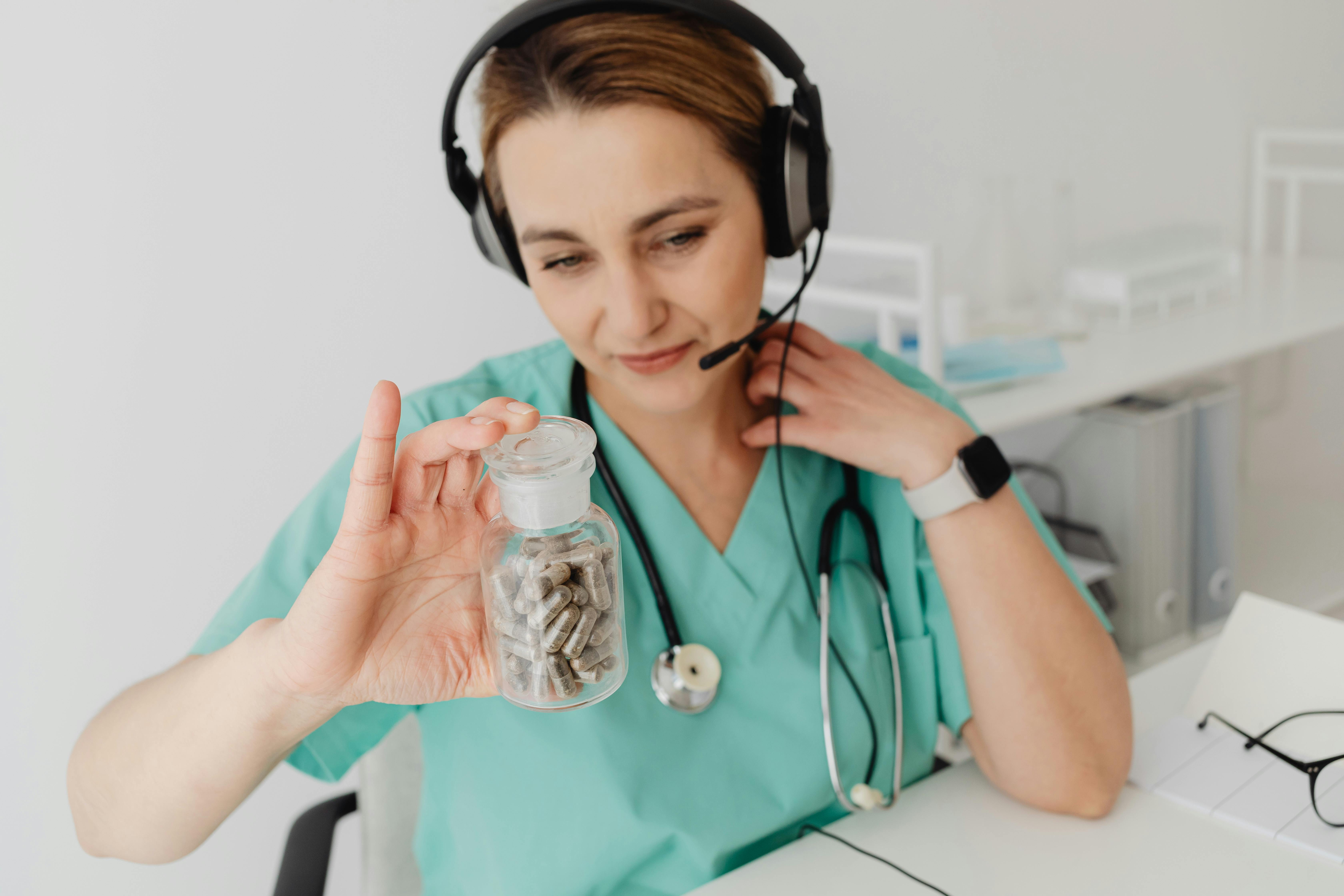 Medical professional wearing headphones holding a medicine bottle during a telehealth consultation