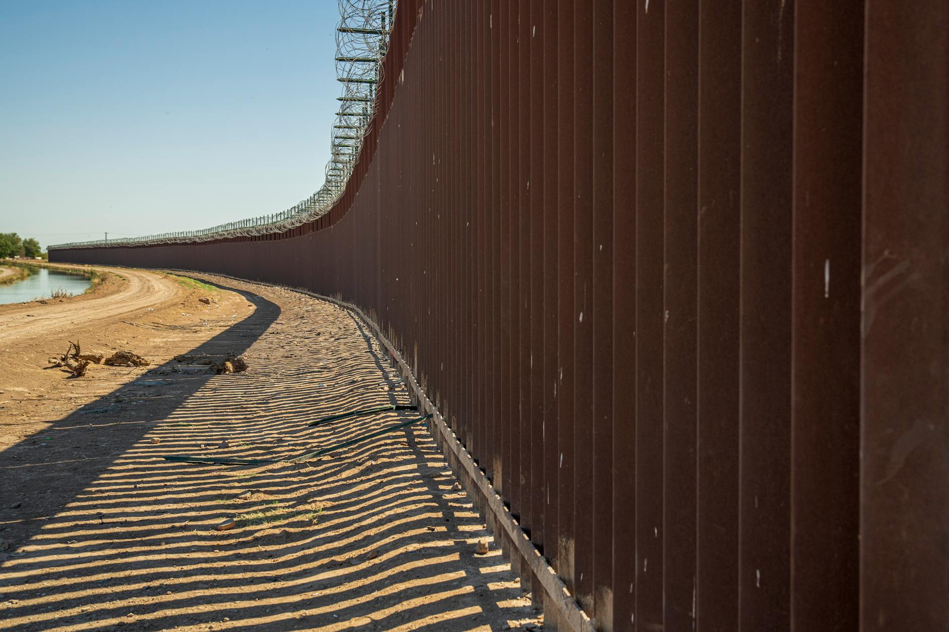 Steel border wall stretching across desert terrain under clear skies at the US-Mexico border