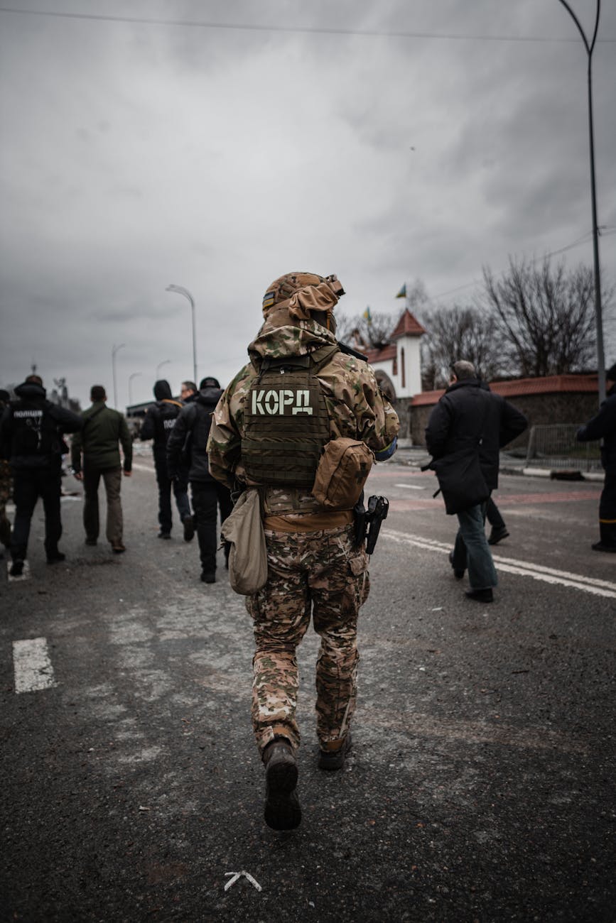 A soldier in camouflage and tactical gear walking down a street in Borodyanka, Ukraine, amidst a group of people