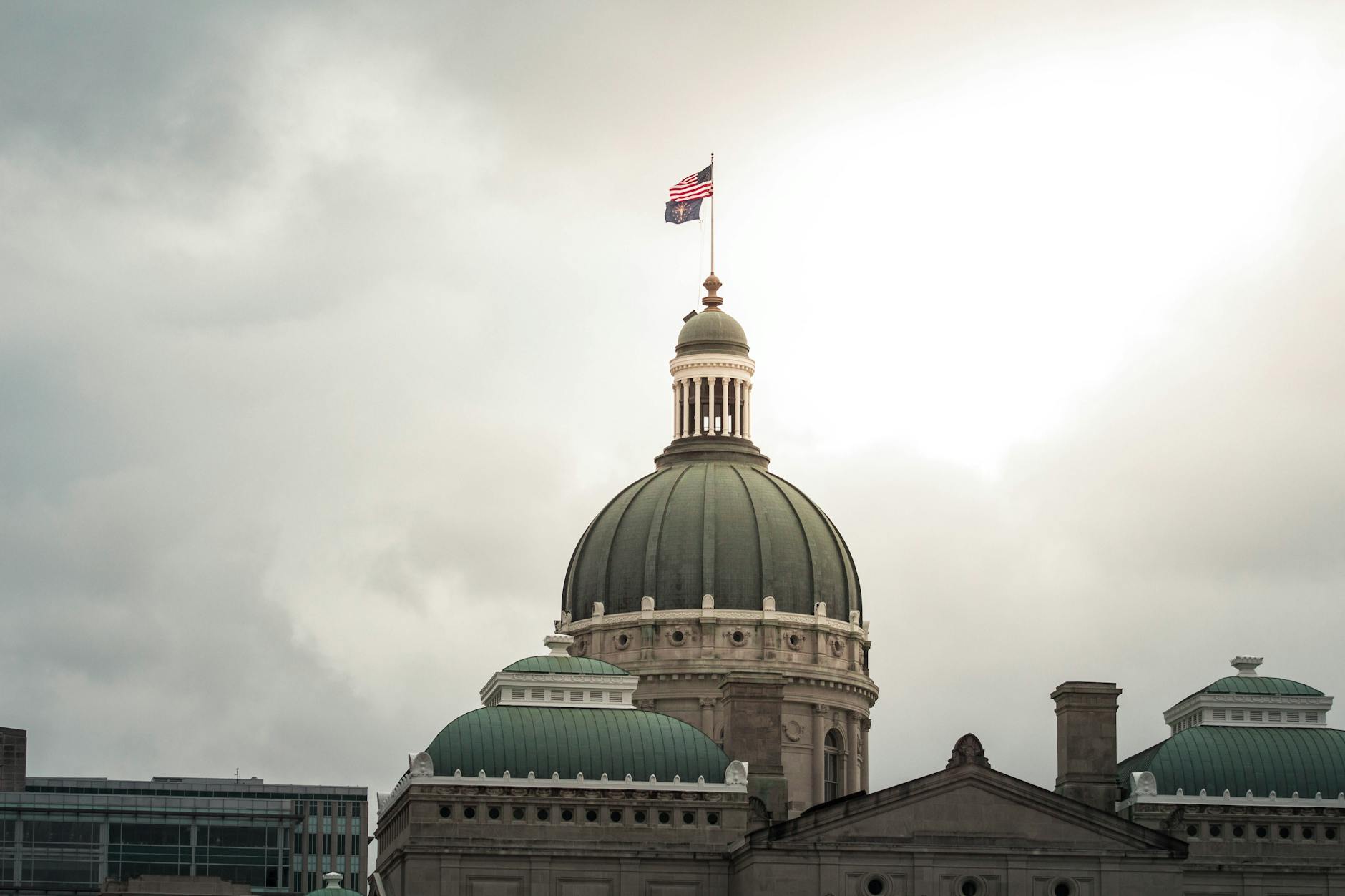 American flag flying above the Indiana Statehouse dome in Indianapolis under a cloudy sky.