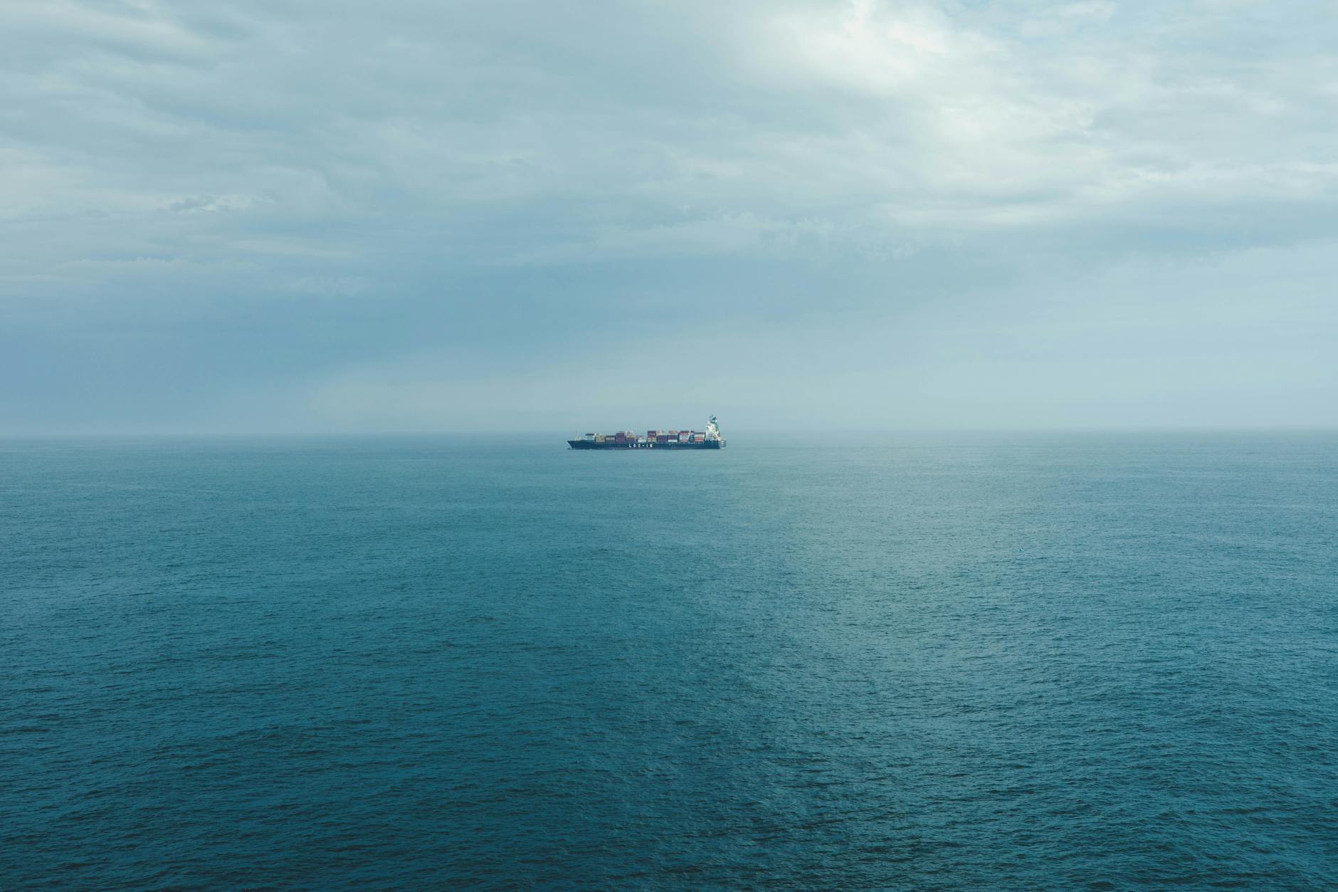 A solitary cargo ship sails on a calm ocean under a cloudy sky