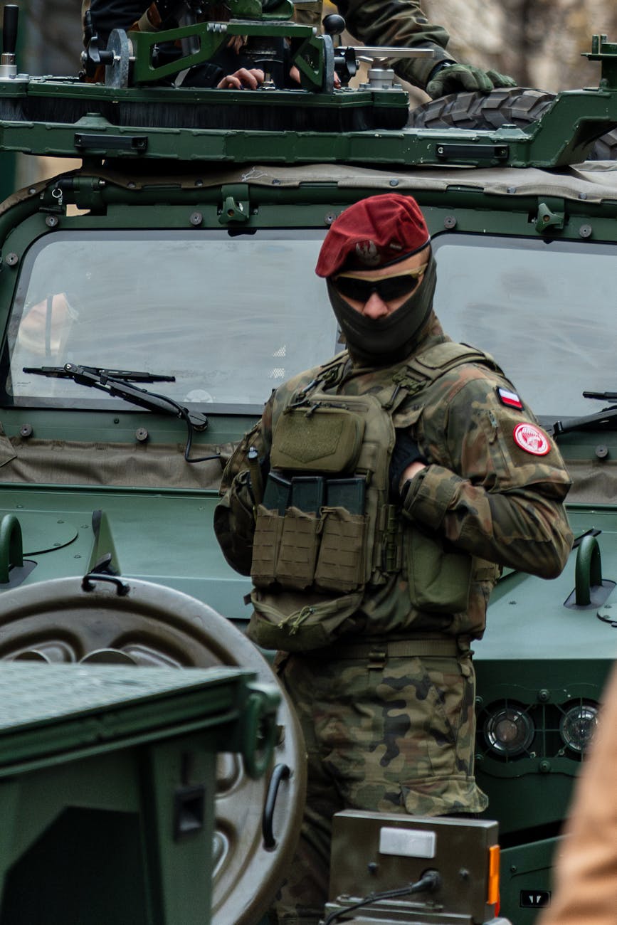 A Polish soldier in uniform stands in front of a military vehicle, illustrating European NATO posture amid US troop withdrawal debate