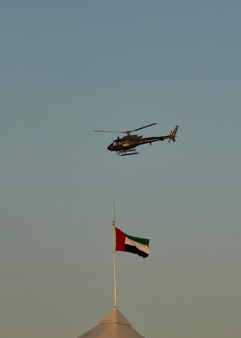 Military helicopter flying above UAE flag against clear sky
