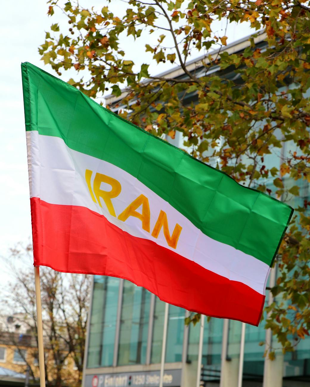Iranian flag in vibrant colors waves against an urban backdrop, capturing national pride.