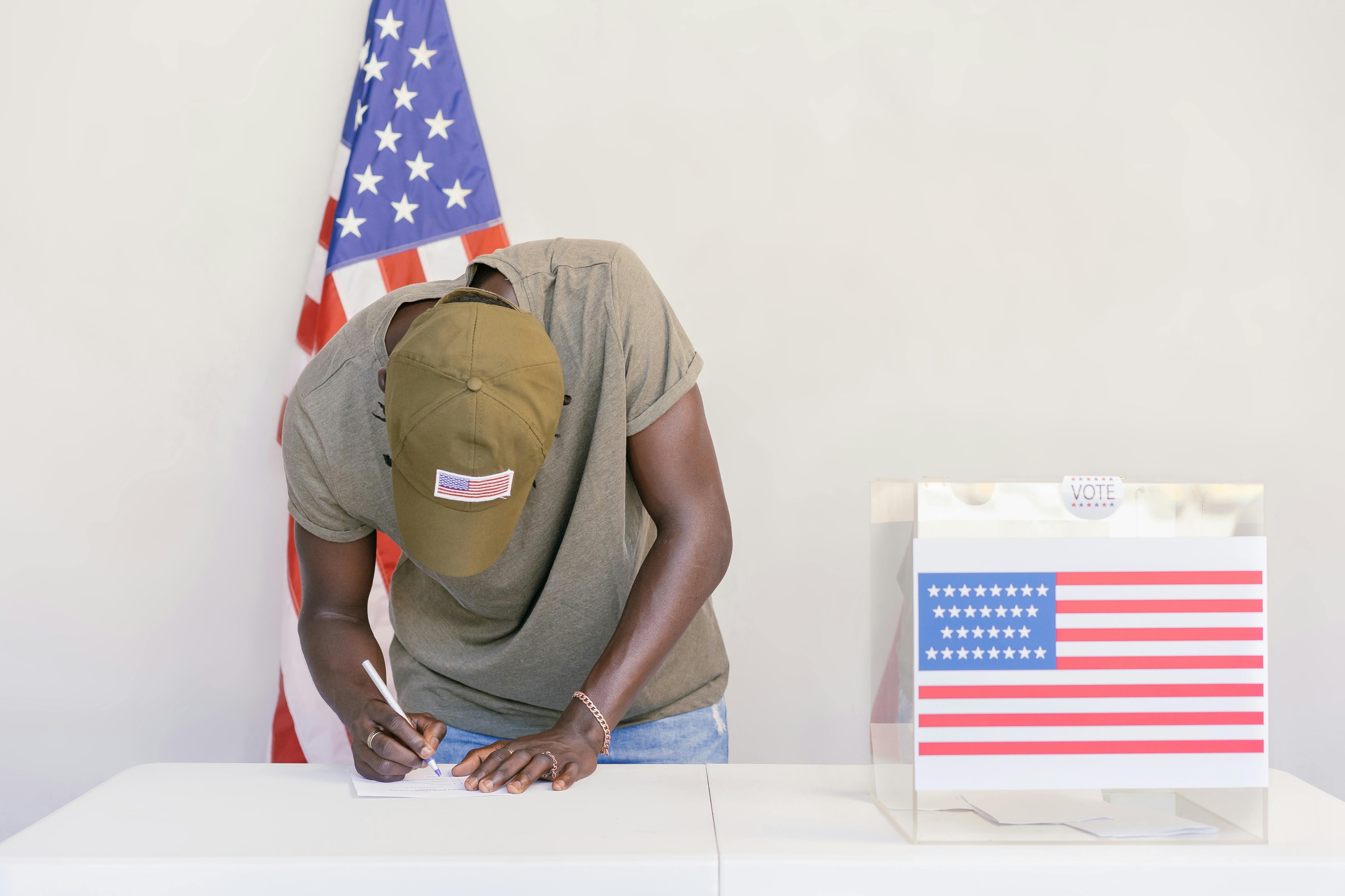 Man casting vote at polling station with American flag in background