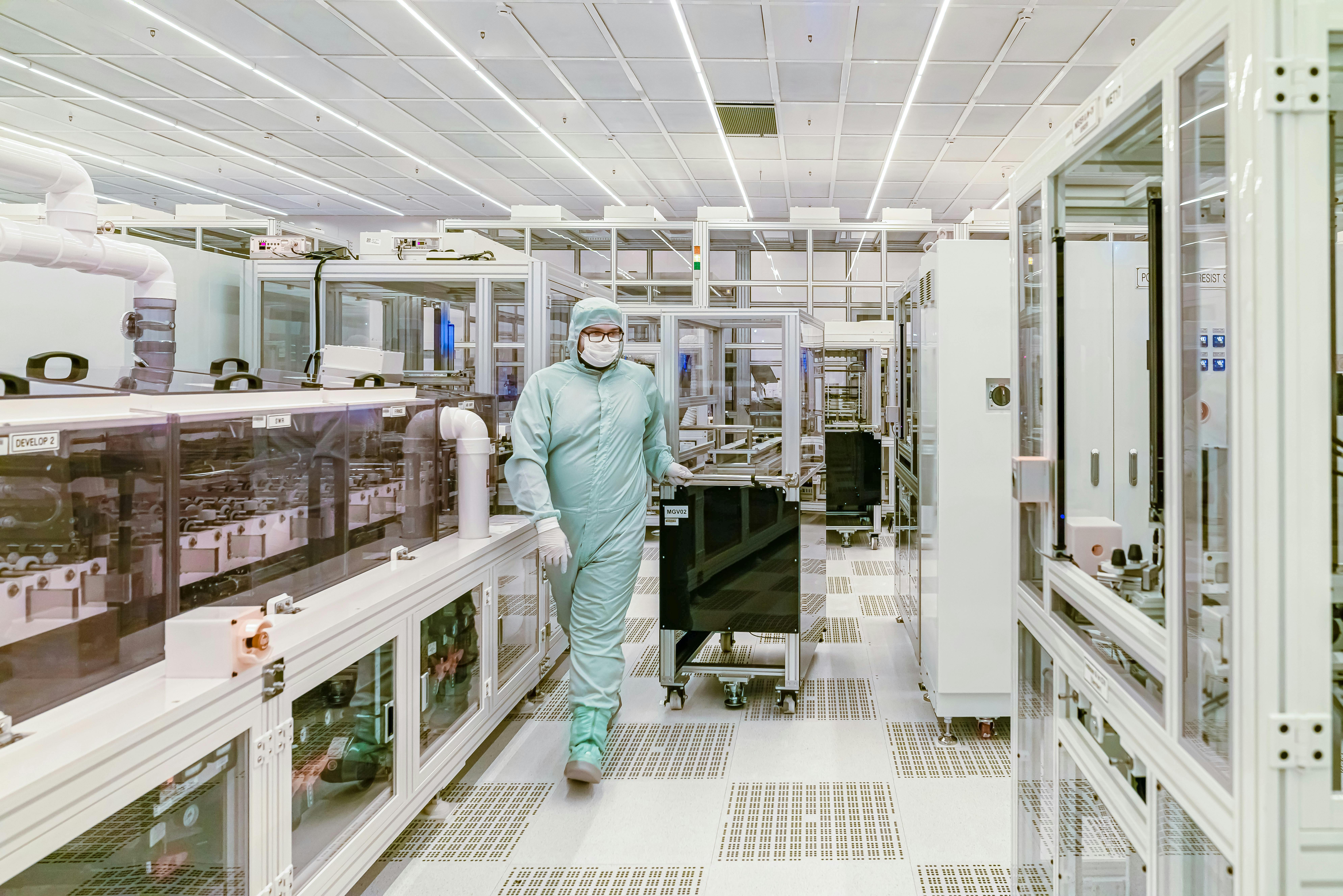 Scientist in protective gear walking in a high-tech cleanroom semiconductor fabrication facility