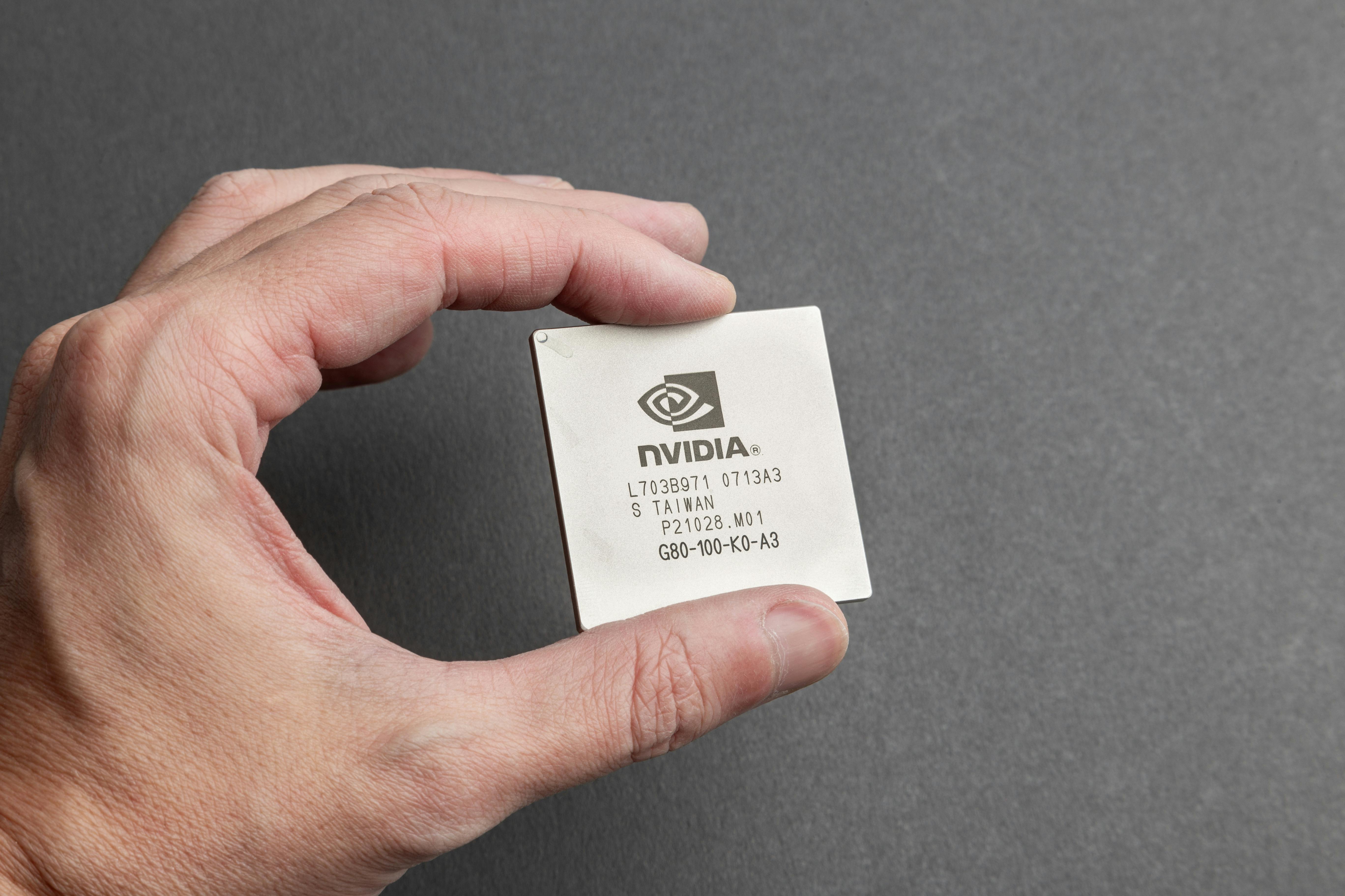A close-up view of a person holding an Nvidia chip with a gray background