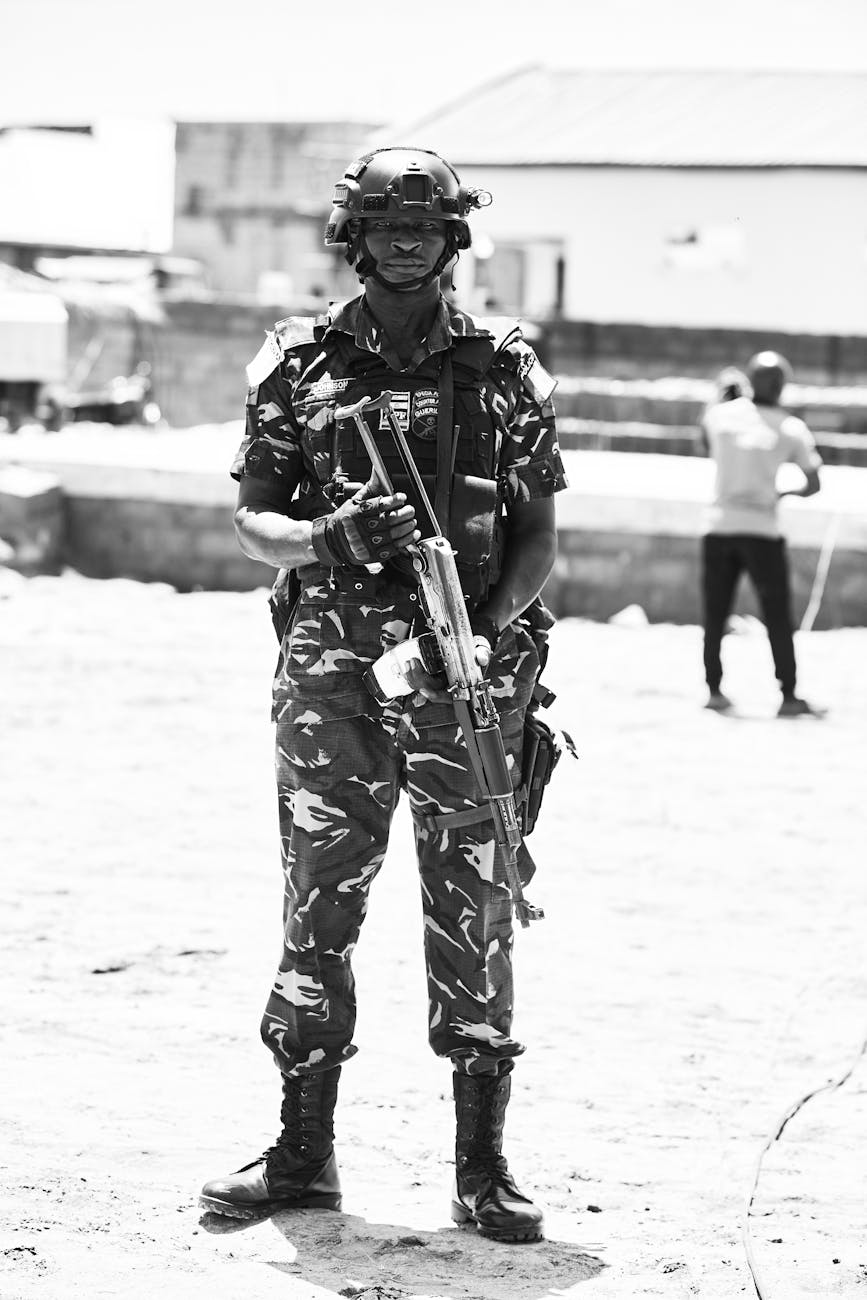 Black and white photo of a Nigerian soldier equipped with tactical gear standing outdoors.
