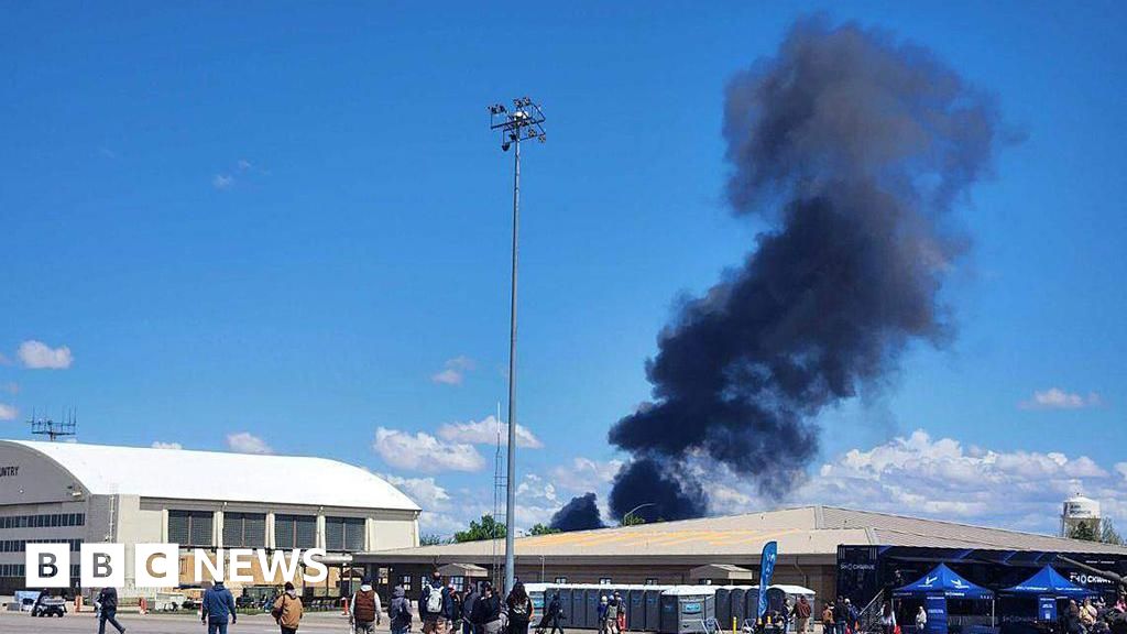 Black smoke rises into a blue sky over a US military base