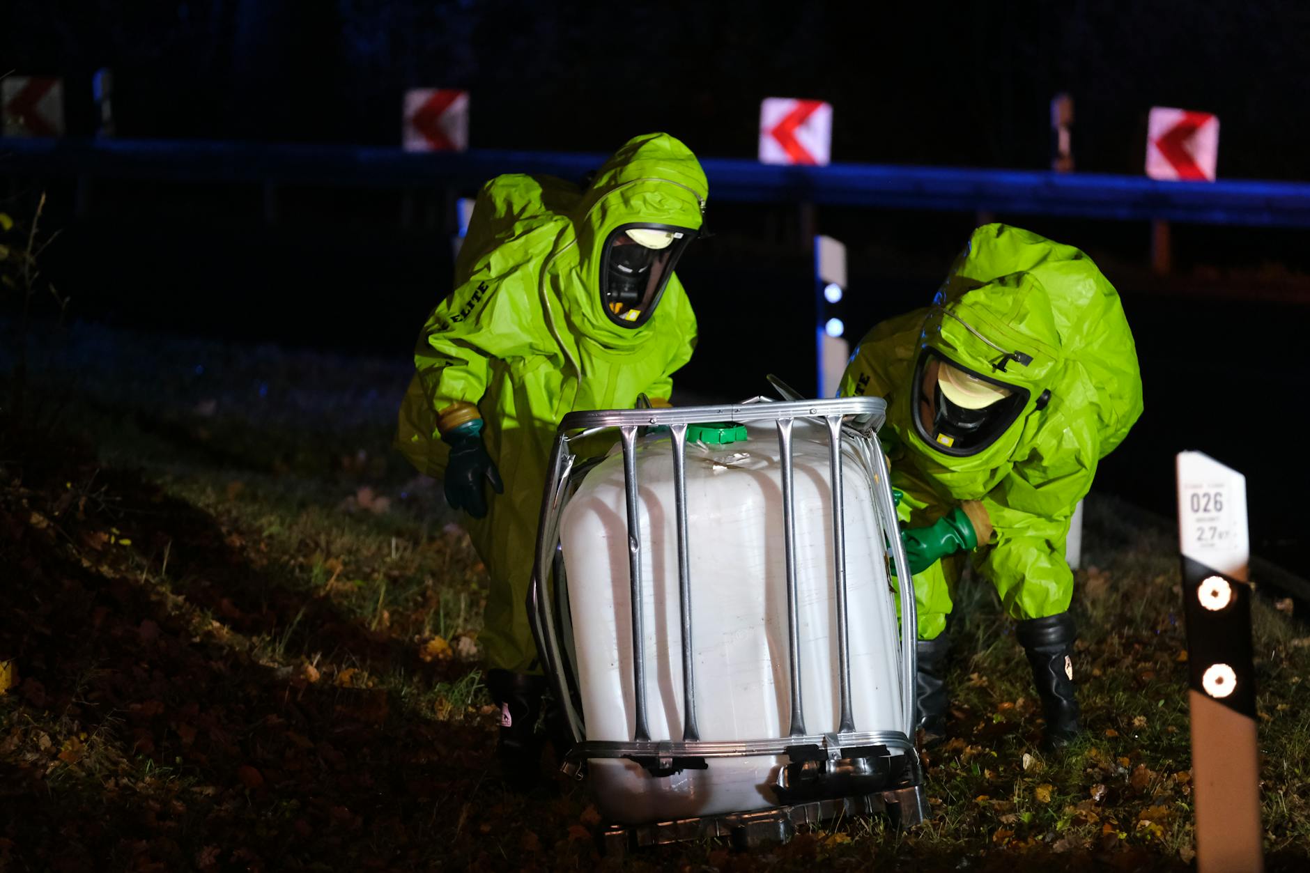 Firefighters in hazmat suits secure a damaged container during an emergency response.