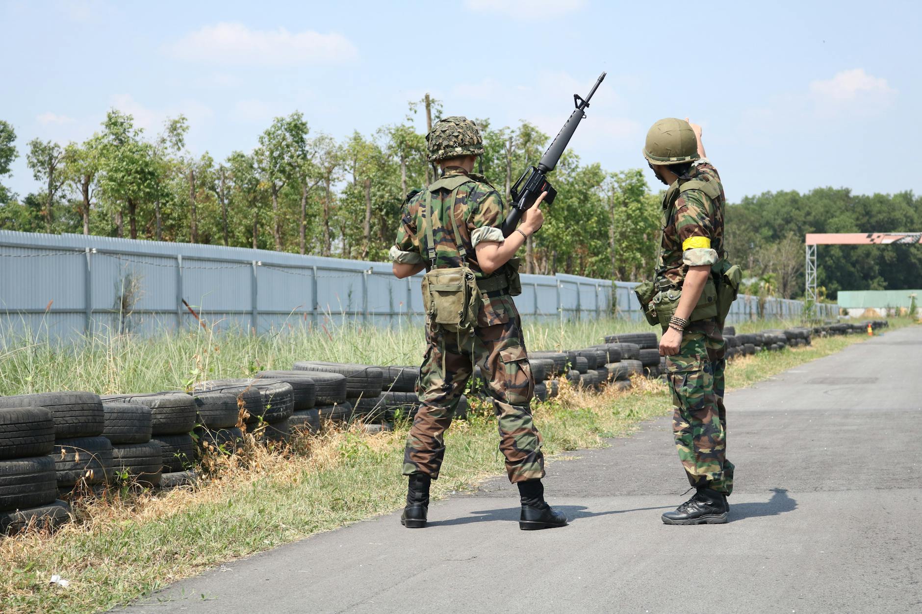 Two soldiers in camouflage uniforms stand armed on a training field.