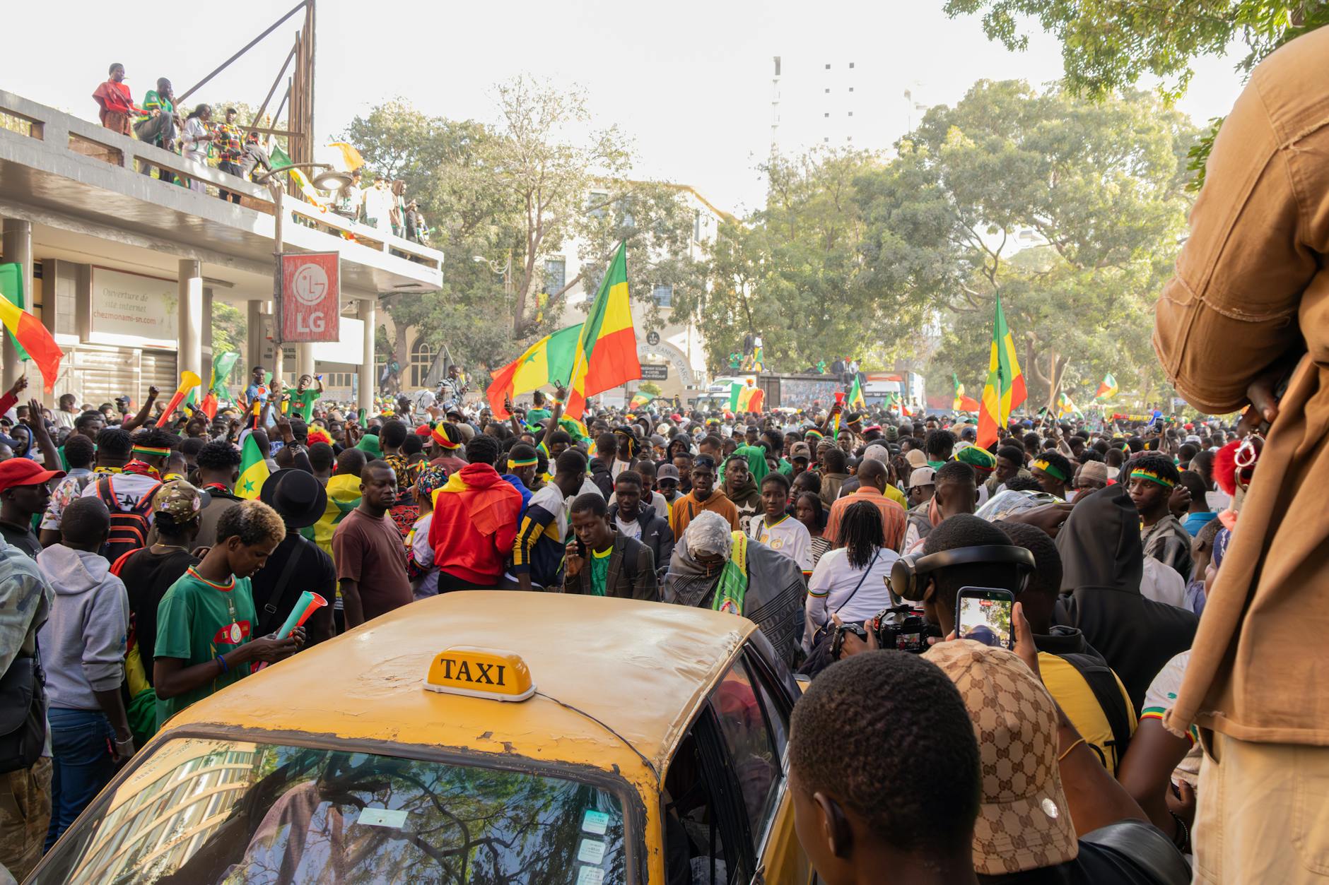 A lively street scene in Dakar, Senegal, with a crowd celebrating and waving flags.