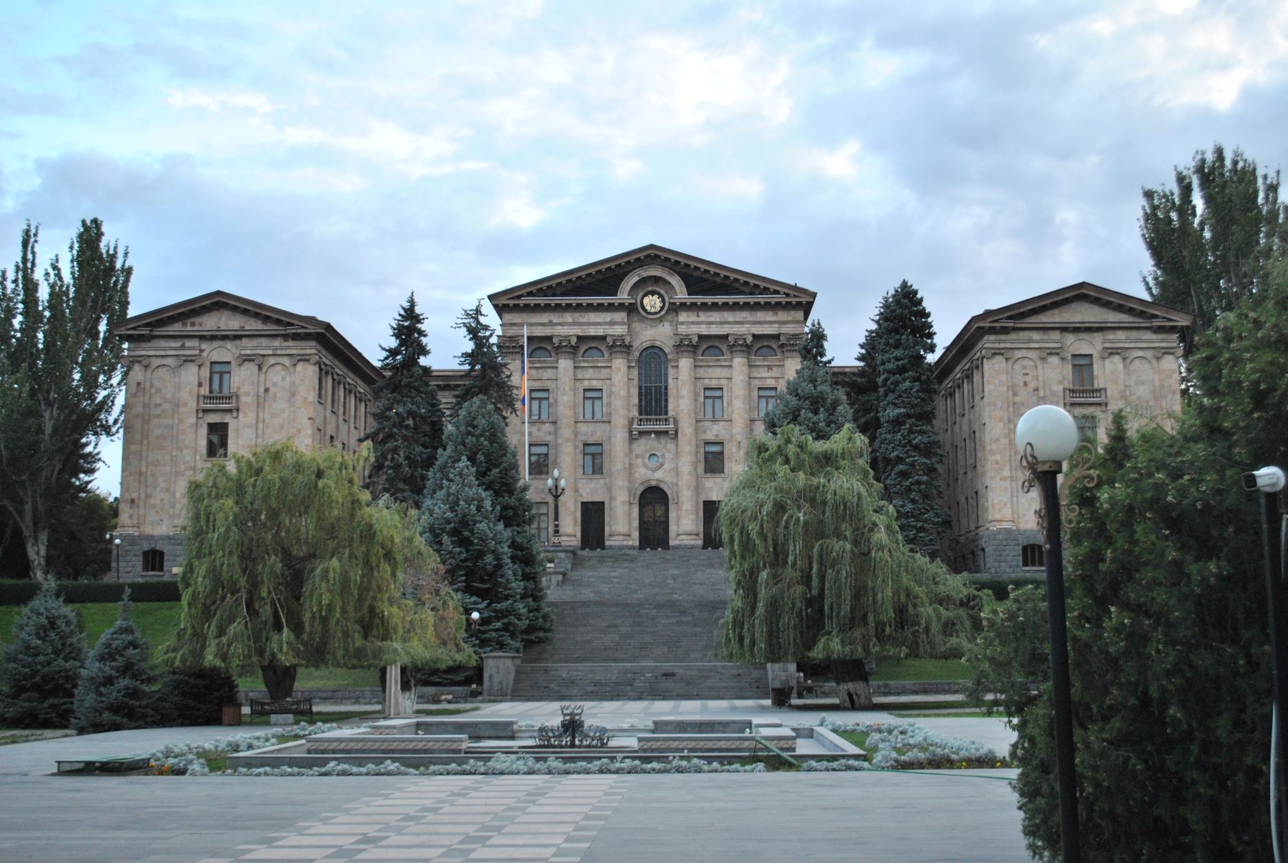 Historic government building in Yerevan framed by greenery under a cloudy sky.